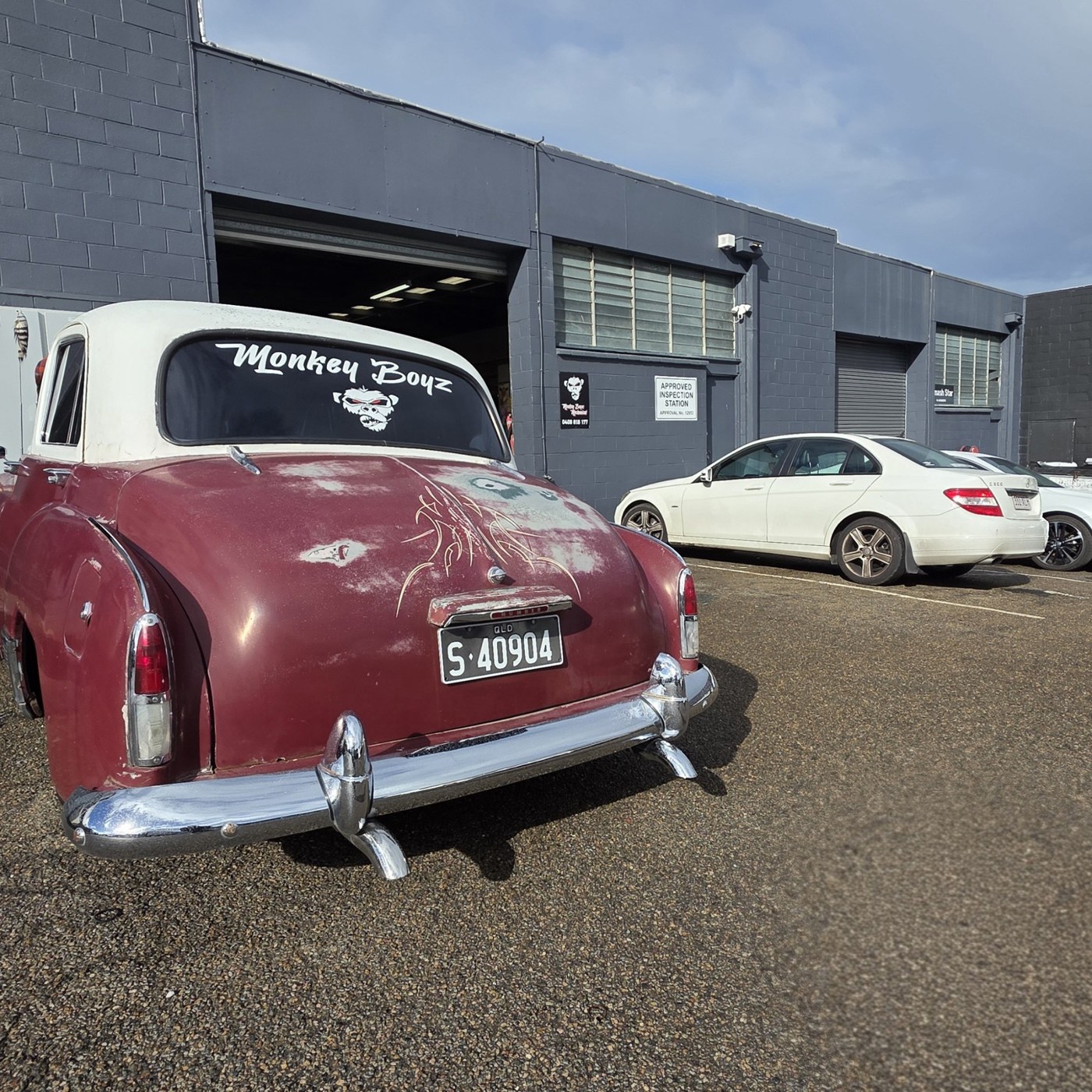 A red classic car and white sedan outside the Monkey Boyz workshop